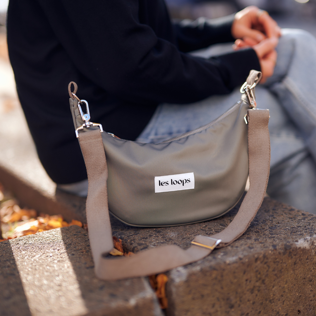 Die halbmondförmige Crossbody Bag Graugrün ist robust und wasserabweisend aus recycelten Stoffen, die perfekte Begleiterin im Alltag